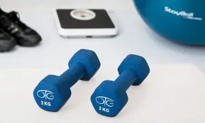 Dwa niebieskie hantle po 2 kg, waga, buty sportowe i piłka gimnastyczna.