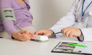 Lekarz mierzy ciśnienie pacjentce, która jest w stanie przedrzucawkowym. Na stole leżą zdjęcia USG.