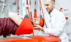 Fizjoterapeuta pomaga pacjentowi z rozszczepem kręgosłupa w terapii wiszącej.