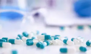 Kapsułki z antybiotykami w kolorze białym i turkusowym leżą na białej powierzchni.