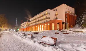 Sanatorium nocą, ośnieżone ławki i chodnik przed budynkiem.