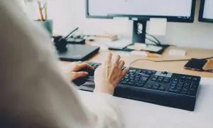 Dłonie piszą na klawiaturze, za nimi monitor. Szybkie załatwienie sprawy, może zwolnienie lekarskie online?