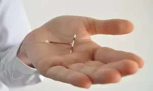Dłoń trzyma spiralę antykoncepcyjną w kształcie litery T z miedzianym drutem i nitkami.