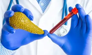 Lekarz w niebieskich rękawiczkach trzyma model trzustki i probówkę z krwią, sugerując badanie poziomu amylazy.