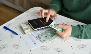 Ręce liczą pieniądze i dokumenty ZUS. Na stole leżą polskie banknoty, kalkulator i karta legitymacyjna emeryta-rencisty, co sugeruje sprawy związane z rentą chorobową.