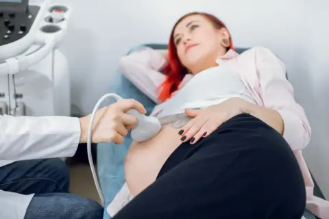 Kobieta w ciąży z rudymi włosami przechodzi badanie USG. Lekarz wykonuje badanie, aby wykluczyć zespół Edwardsa.