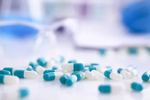 Kapsułki z antybiotykami w kolorze białym i turkusowym leżą na białej powierzchni.