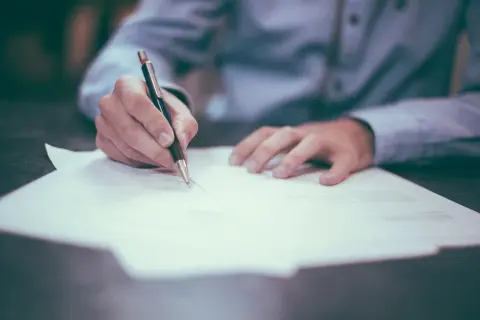 Dłoń pisząca długopisem na papierze, symbol precyzji i dbałości o szczegóły, cechy osobowości anankastycznej.