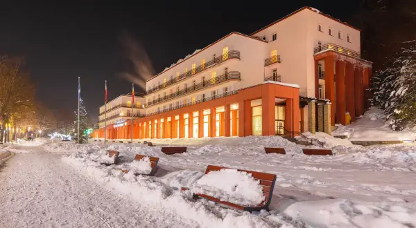 Sanatorium nocą, ośnieżone ławki i chodnik przed budynkiem.