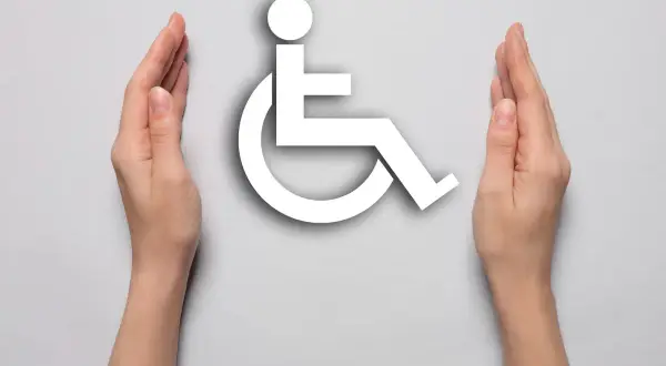 Dwie dłonie otaczają symbol osoby na wózku inwalidzkim, symbolizując wsparcie dla osób, na jakie choroby można dostać orzeczenie o niepełnosprawności.