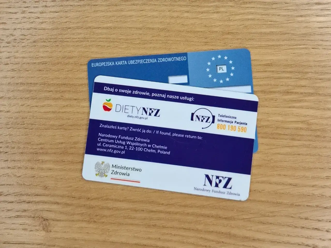 Europejska karta ubezpieczenia zdrowotnego i karta DIETYNFZ. Dwie karty na drewnianym tle.