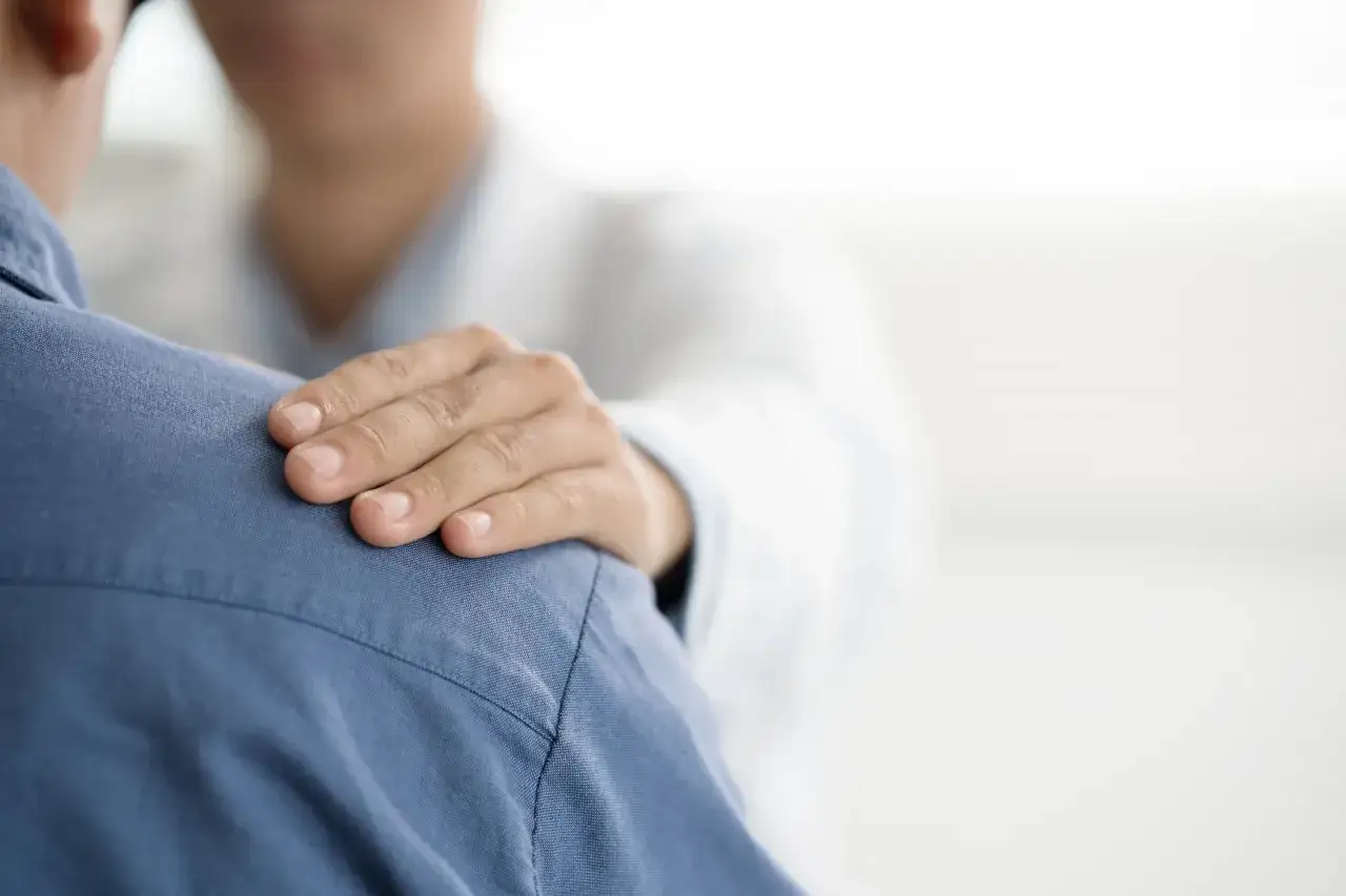 Dłoń lekarza na ramieniu pacjenta. Czy do psychiatry potrzebne jest skierowanie? Wsparcie i troska w gabinecie lekarskim.