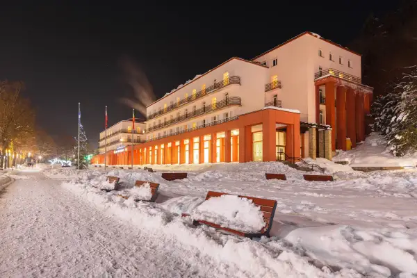 Sanatorium nocą, ośnieżone ławki i chodnik przed budynkiem.