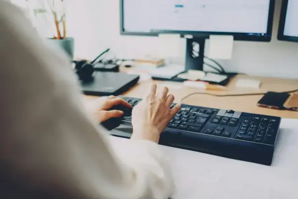 Dłonie piszą na klawiaturze, za nimi monitor. Szybkie załatwienie sprawy, może zwolnienie lekarskie online?