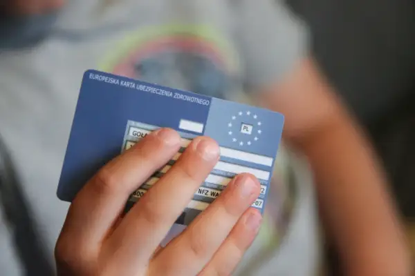 Dziecko trzyma Europejską Kartę Ubezpieczenia Zdrowotnego. To ważny dokument, gdy podróżujesz po Europie. Ekuz co to? To Twoje ubezpieczenie zdrowotne.