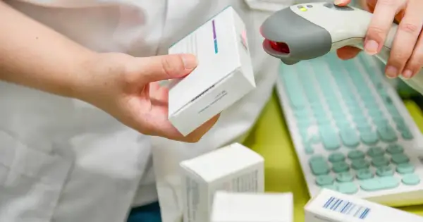 Farmaceuta skanuje lek, pokazując, ile ważna jest recepta. W tle klawiatura i inne opakowania.