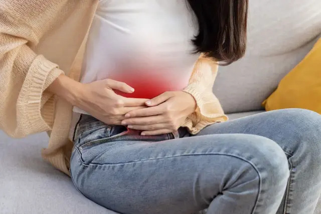 Kobieta trzyma się za brzuch, gdzie widoczny jest czerwony obszar bólu. Może to być objaw zapalenia wyrostka robaczkowego, wymagający pilnej diagnostyki.